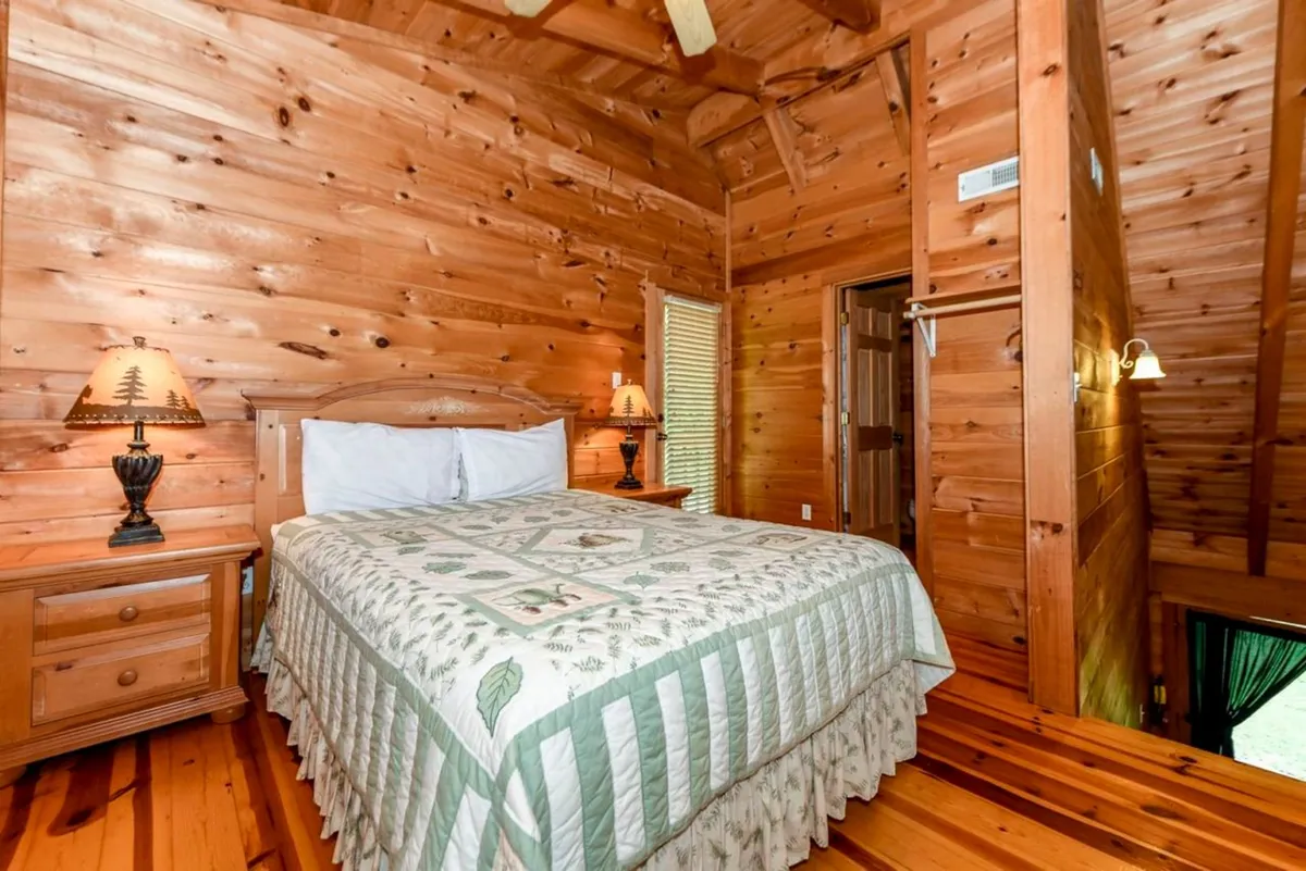 A serene bedroom with a bed adorned in a floral quilt, accompanied by bedside lamps and set against wooden walls. The mood is quiet and tranquil, fostering a sense of retreat.