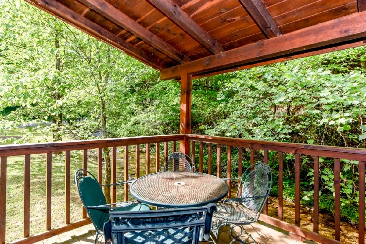 A peaceful wooden deck with a metal dining table and chairs, surrounded by greenery. The space offers an inviting spot for outdoor dining, relaxation, and observing nature.