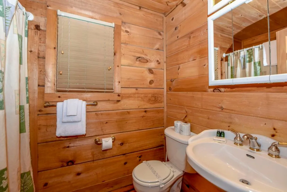 A welcoming bathroom with wooden walls, a sink, mirror, toilet, and a shower curtain. The space is practical yet comfortable, ideal for refreshing after a long day.